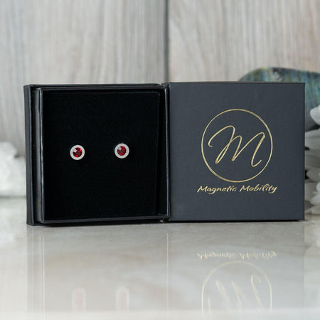 Magnetic Mobility Birthstone Stud Earrings featuring red Swarovski crystals, elegantly presented in a black box with Magnetic Mobility logo. These magnetic back earrings provide stylish pain relief.